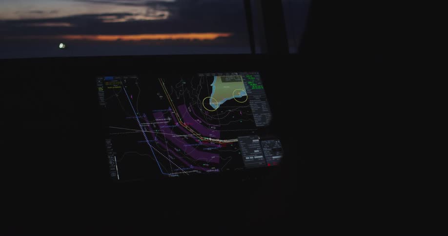 A ship's electronic chart plotter navigates through dark waters with the glow of sunset visible on the horizon