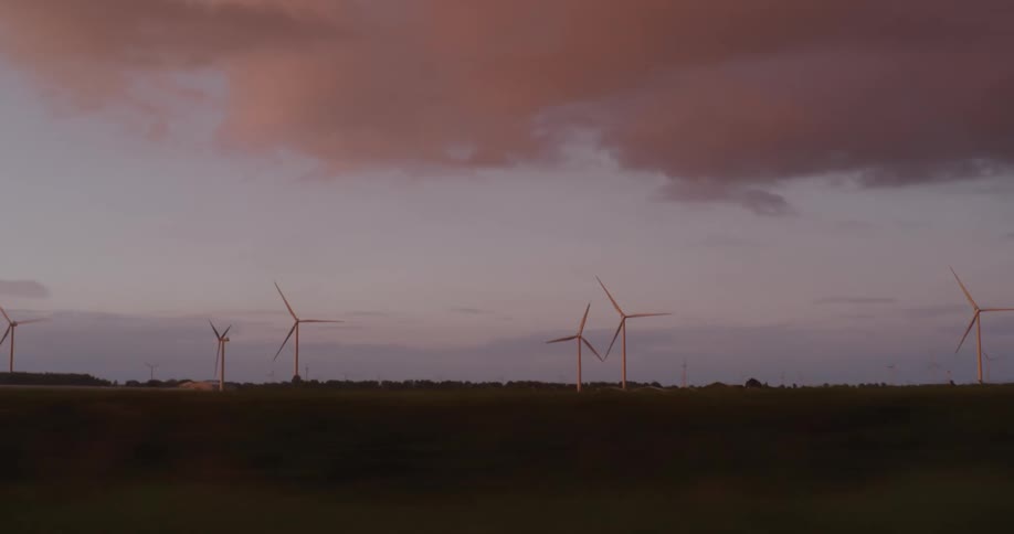 Wind turbines spin gracefully on the horizon during a stunning sunset, as seen from a moving vehicle