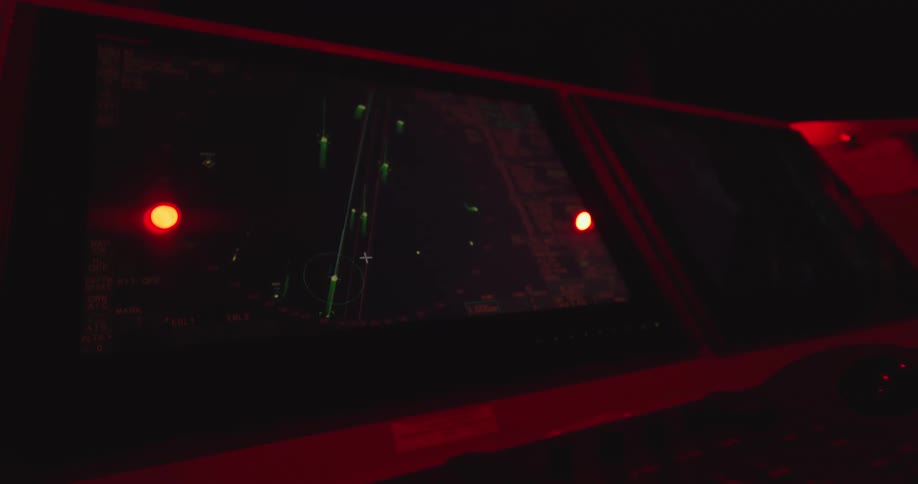 A ship's marine radar navigation screen displays nearby vessel traffic on the bridge at night, illuminated by red light