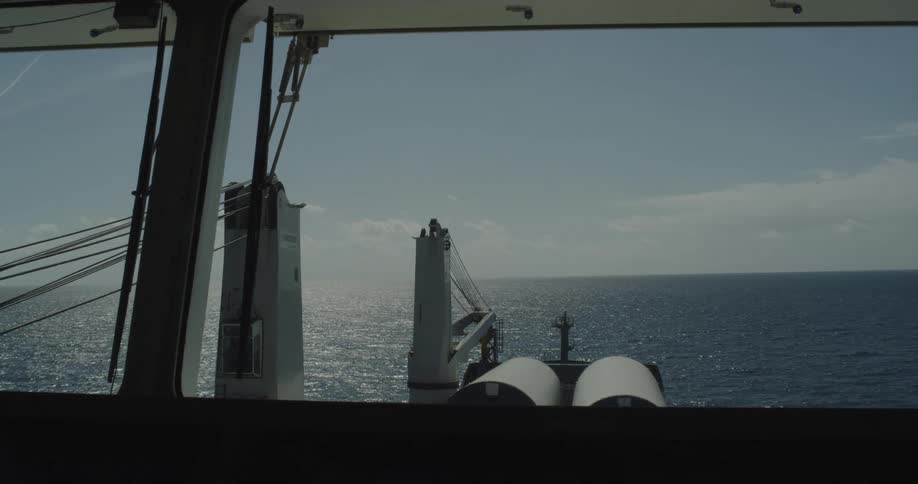 POV from a cargo ship's bridge as it sails on a sunny day across the sparkling blue ocean