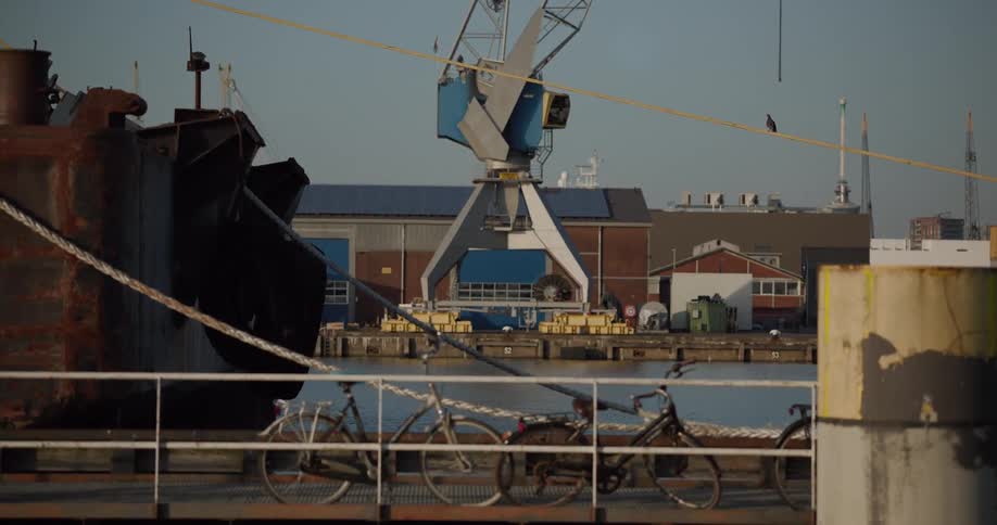 Static shot of an industrial harbor with bicycles parked on a dock next to a rusty ship