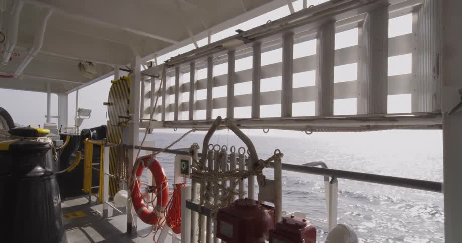View from the deck of a large ship sailing on the open ocean with life-saving equipment visible