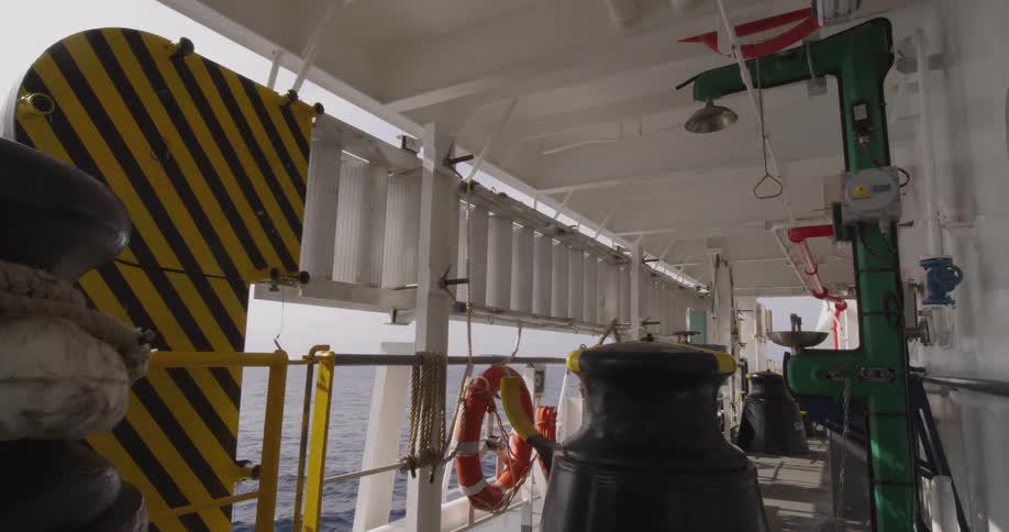 A static view of a ship's deck with safety equipment, including a lifebuoy and ladder, while sailing on the open ocean