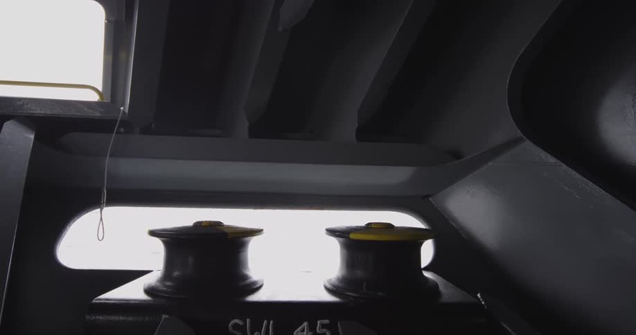 View from inside a large vessel showing two mooring bitts with the bright open ocean passing by in the background