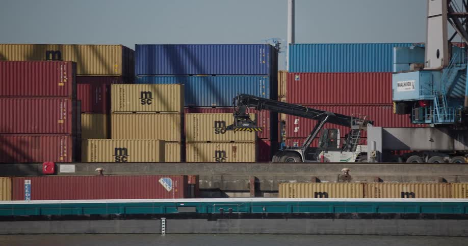 A container handler skillfully stacks large shipping containers at a bustling commercial port