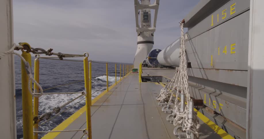 A steady point-of-view shot from the deck of an industrial vessel as it sails across the open sea on a hazy day