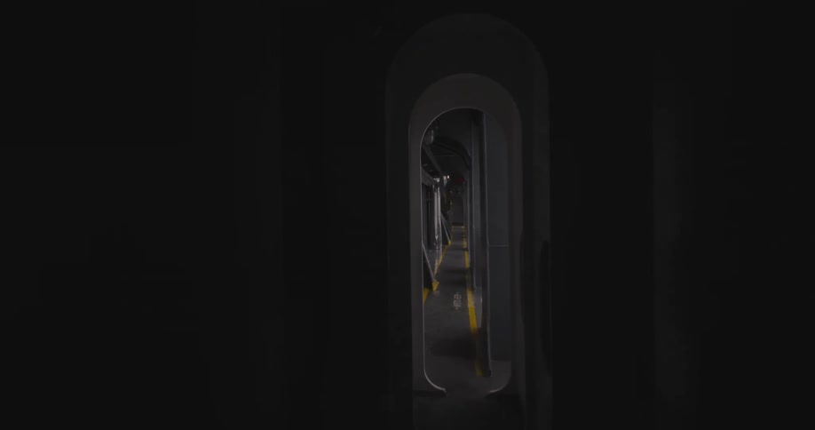 A slow zoom-out from a dark, narrow opening reveals a long and empty industrial corridor