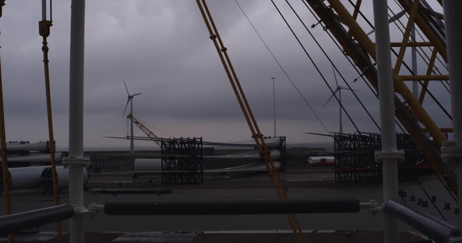 A static shot of a wind turbine blade depot with spinning turbines in the background under a dark, cloudy sky