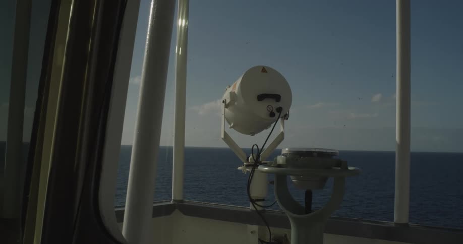 View from a ship's bridge showing navigation equipment and the vast open ocean on a sunny day