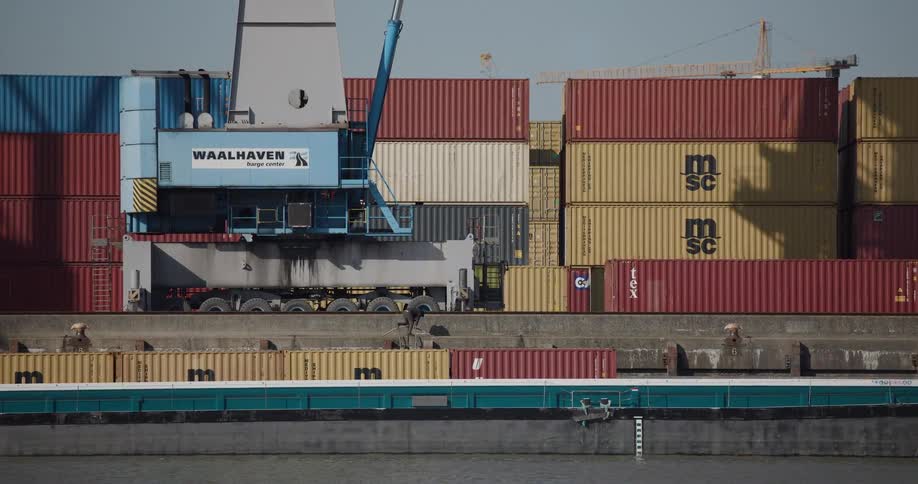 A worker walks across a cargo barge at the industrial Waalhaven shipping port with stacked containers in the background