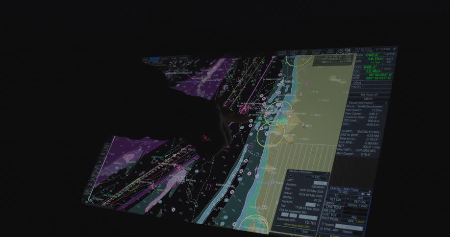 A navigational officer plans a ship's route on a modern touchscreen ECDIS system in a dark control room
