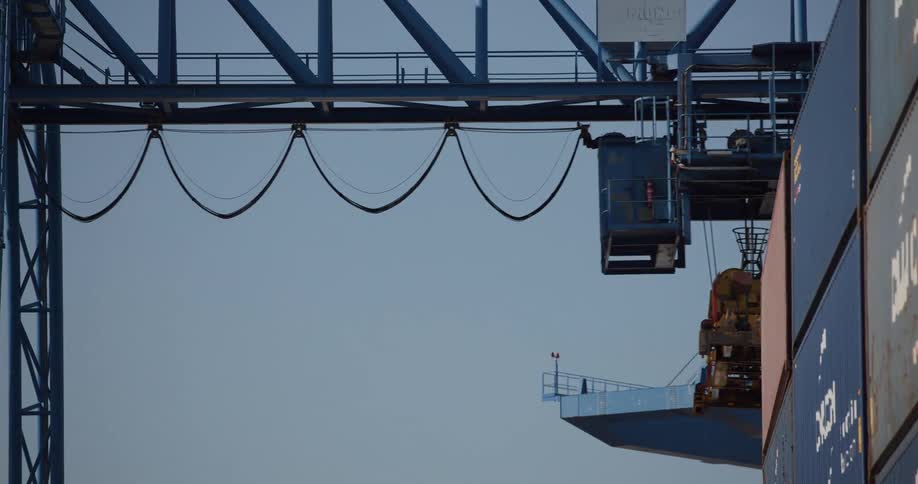 Close-up view of a gantry crane trolley moving along the beam to position itself over shipping containers at a port