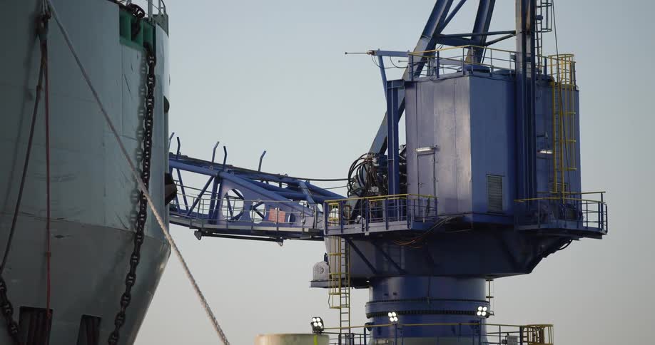 A static close-up shot of a large blue industrial crane connected to a cargo ship docked in a harbor