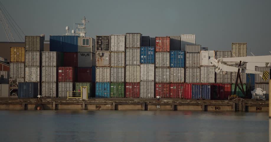 A static shot of colorful cargo shipping containers stacked high on an industrial dock next to the water