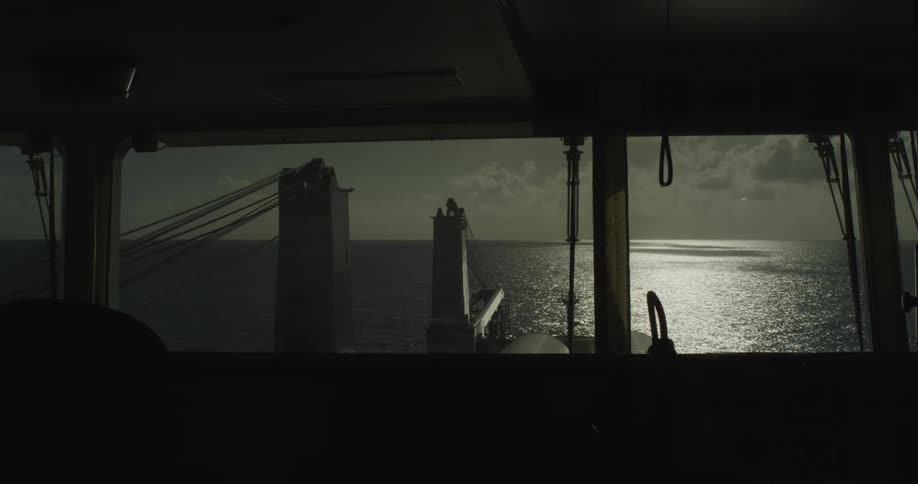 View from the silhouetted bridge of a cargo ship as it sails across the shimmering open ocean