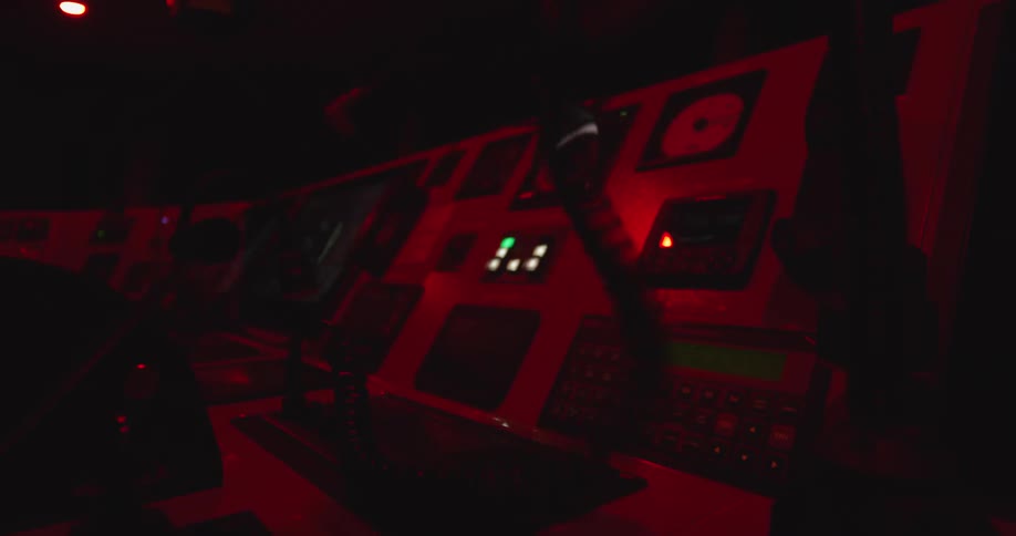A person's hand operates a complex control panel in a dark room illuminated by eerie red lights