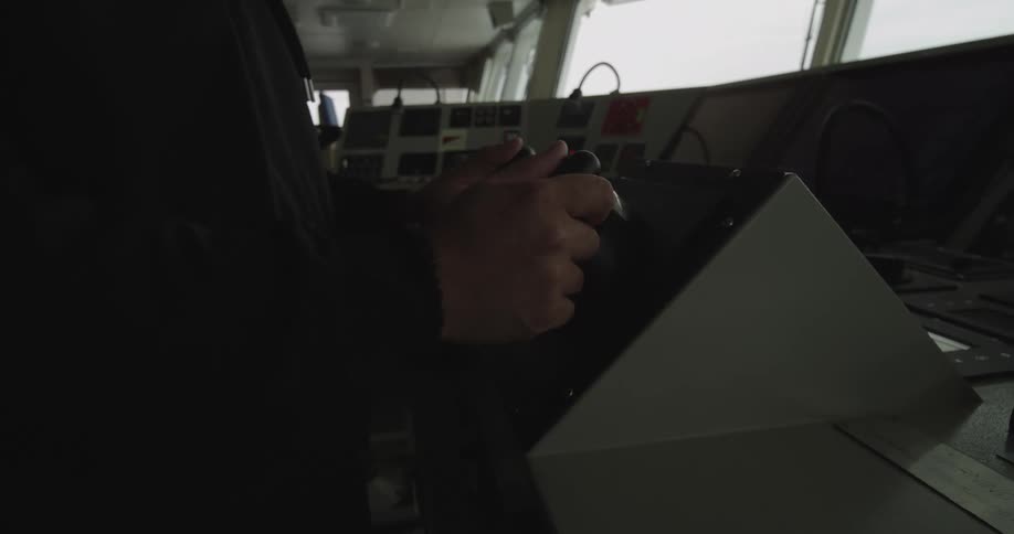 Close-up of a ship navigator's hands operating a control lever on the dimly lit bridge