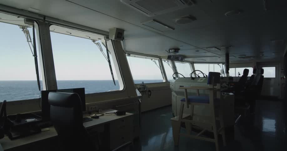 The quiet, empty bridge of a large ship sails across the calm ocean on a clear day