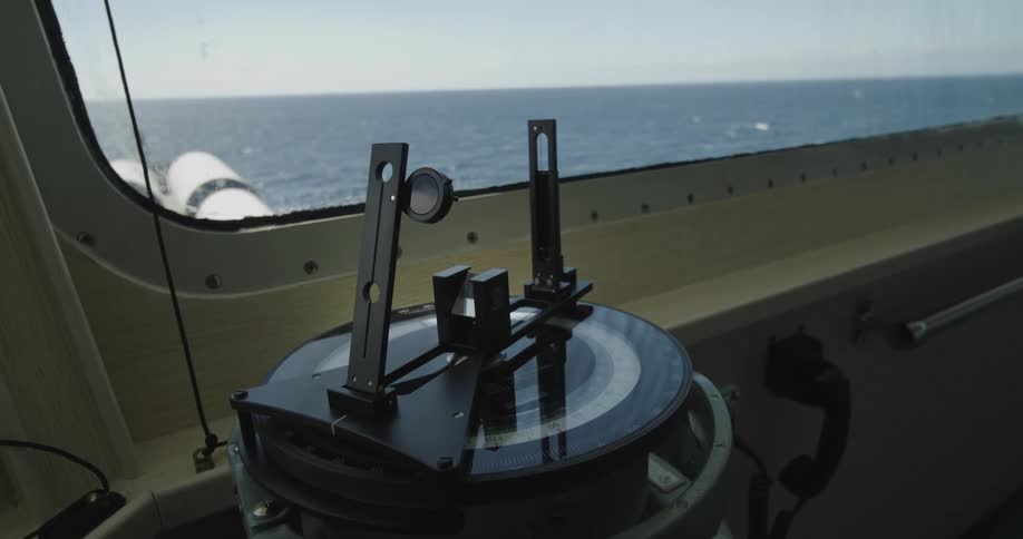 A ship's magnetic compass on the navigation bridge with the open ocean visible through the window