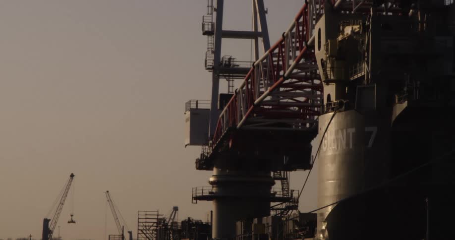 A massive crane vessel named Giant 7 sits docked in an industrial shipyard during a hazy sunrise