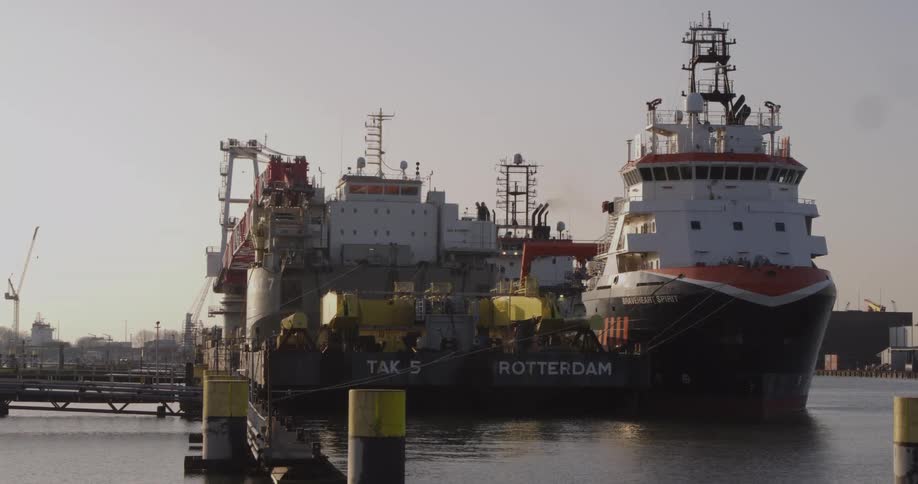 Two massive industrial vessels are docked side-by-side at a pier in a calm commercial harbor