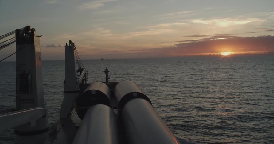 View from a cargo ship carrying large industrial pipes as it sails across the ocean into a beautiful sunset
