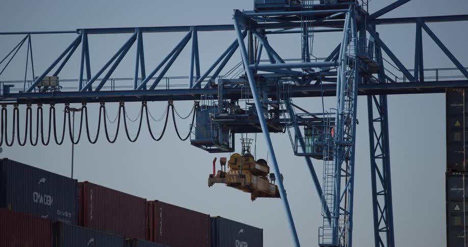 A close-up shot of a massive gantry crane at a shipping port, with the operator visible in the cabin, ready to move cargo containers
