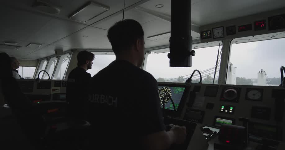 Ship's officers at work on the bridge, steering the vessel through a waterway on an overcast day