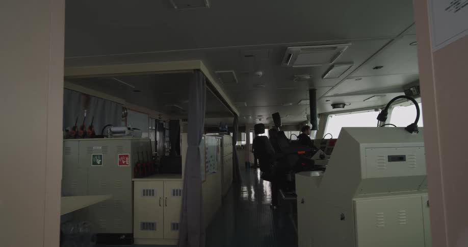Wide interior view of the navigation bridge on a large ship with crew members on duty