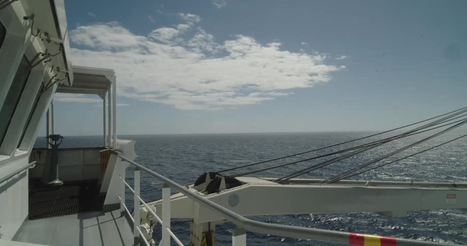 A serene, static view of the open ocean from the deck of a sailing ship on a sunny day