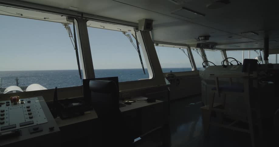 A slow pan reveals the interior of a ship's bridge with a view of the open ocean on a clear day
