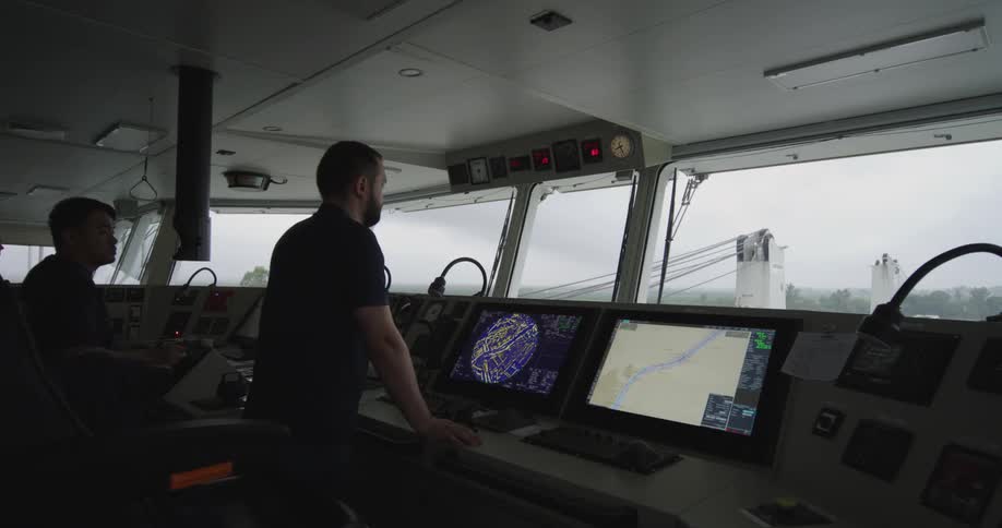 Officers on the bridge of a commercial ship navigate using radar and electronic chart displays on a cloudy day