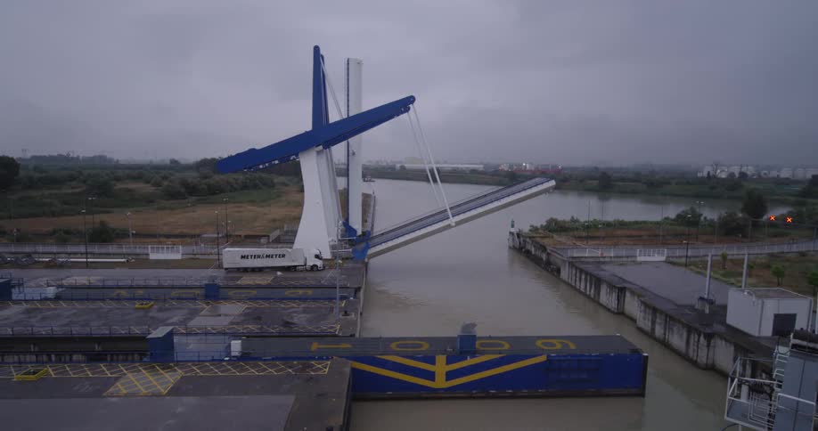 A modern bascule drawbridge slowly lowers over a canal on a cloudy, overcast day
