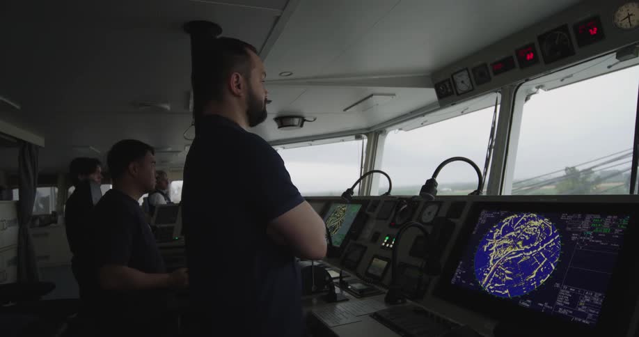 The ship's captain and crew stand watch on the navigation bridge, monitoring radar screens and electronic equipment