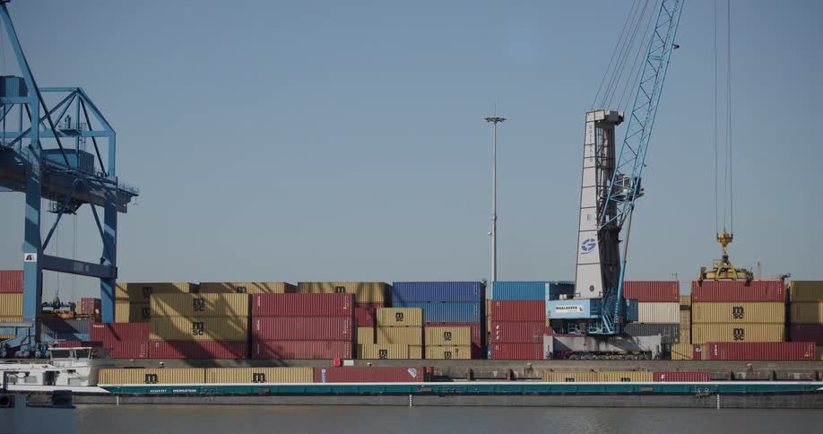 A static view of a large crane moving colorful shipping containers at a busy industrial port by the water