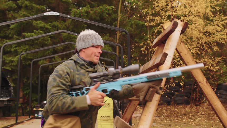 A man participates in a dynamic rifle shooting competition, expertly maneuvering and firing from behind a wooden barricade in an outdoor range