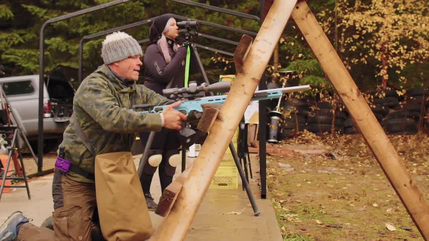 A male shooter in slow motion fires his rifle and navigates a wooden obstacle at a competitive shooting range