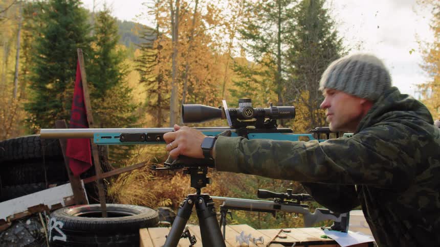 A skilled shooter in camouflage aims his precision rifle on a tripod and adjusts the scope at an outdoor range during autumn