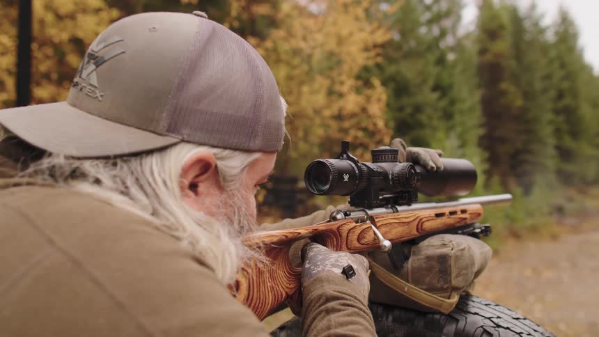 Over-the-shoulder slow motion shot of a man firing a bolt-action rifle at an outdoor range during autumn