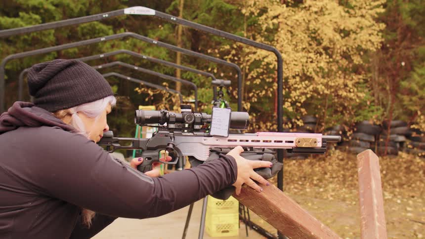 A woman with a custom pink rifle fires and reloads during a shooting competition at an outdoor gun range