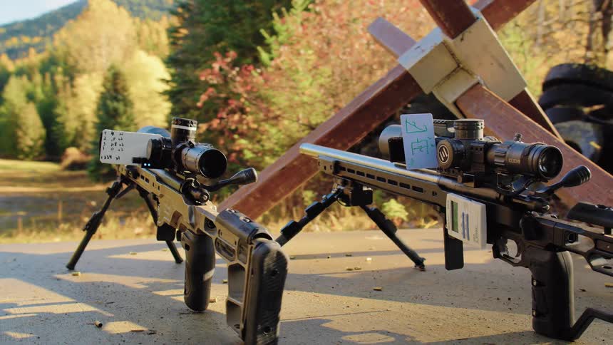 A slow pan reveals two professional sniper rifles set up with scopes on a shooting range table in a sunny, forested autumn landscape