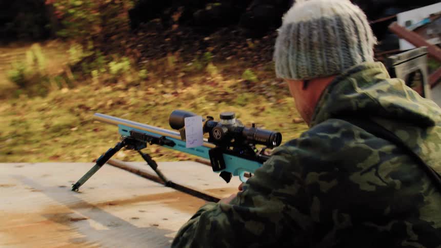 A man in camouflage aims and prepares his long-range rifle at an outdoor shooting range in slow motion