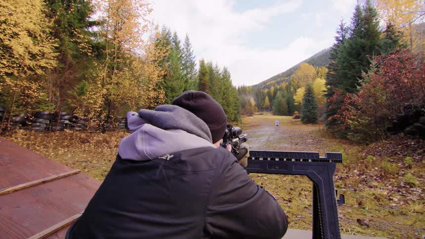 Slow motion pan shot of a man aiming and firing a rifle at a target in a rural outdoor shooting range during the fall