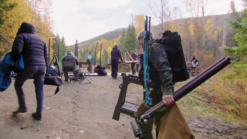 Behind the scenes shot of a film crew setting up production gear in a forest during autumn