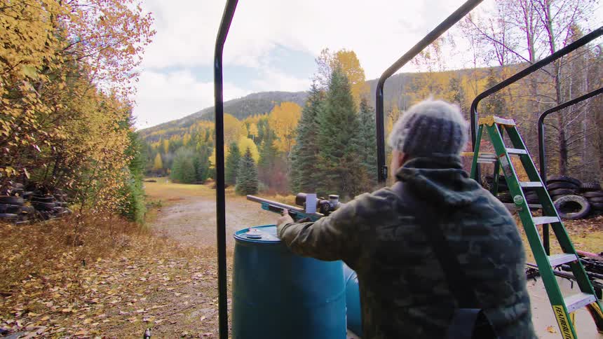 A person fires a scoped rifle multiple times in slow motion at an outdoor shooting range during autumn