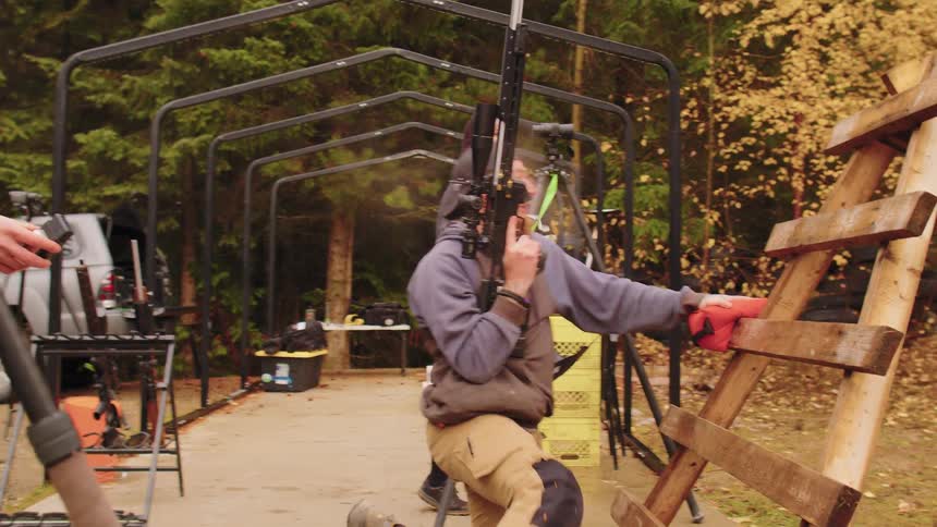 A man at an outdoor shooting range fires a precision rifle in slow motion, with smoke seen coming from the barrel