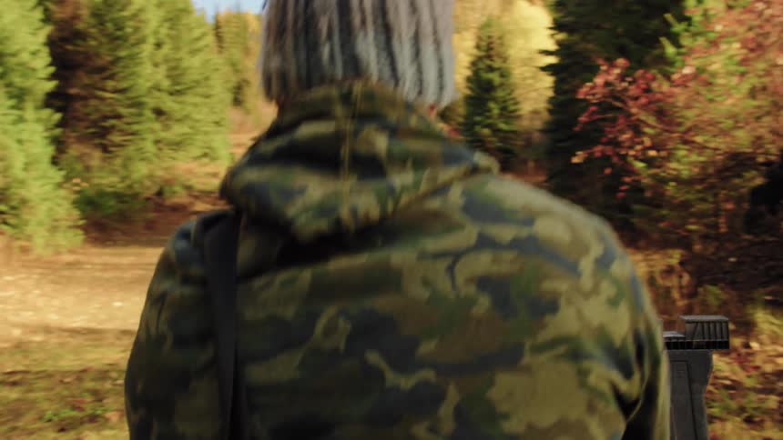 A shooter in camouflage carefully aims his custom blue rifle at a target range, then stands and moves to his next position during a competition