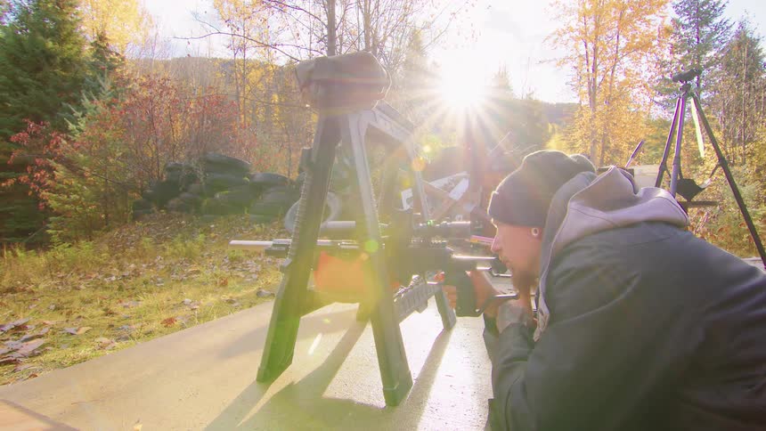 Slow motion dolly shot of a man firing a rifle at an outdoor range with the autumn sun creating a dramatic lens flare