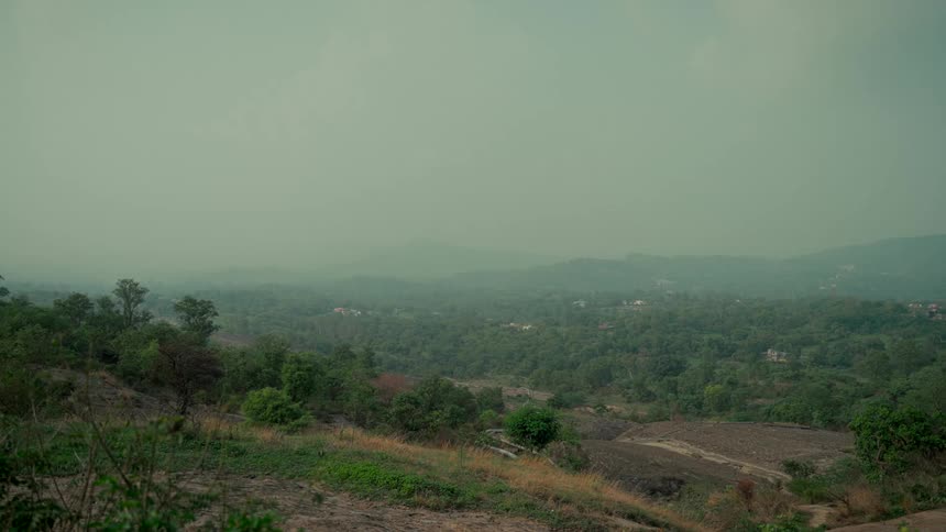 A serene wide shot of a lush green mountain valley under a hazy sky