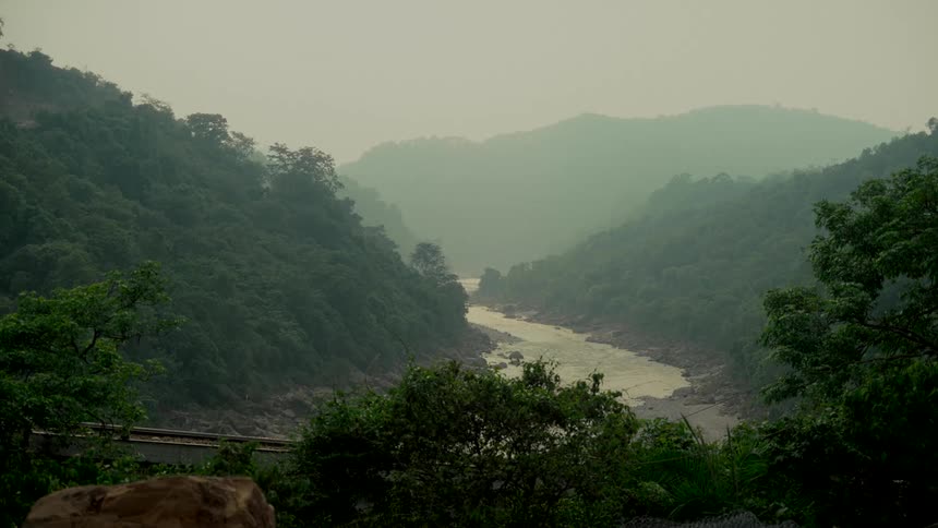 A serene view of a wide river winding its way through a lush, green valley on a foggy, overcast day